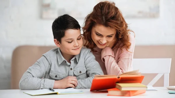 Smiling woman sitting near preteen son and books on blurred foreground — Stock Photo