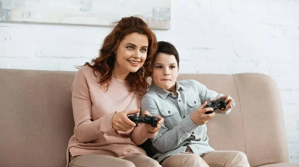 KYIV, UCRANIA - 15 DE ABRIL DE 2019: Mujer sonriente jugando videojuegos con niños en casa - foto de stock