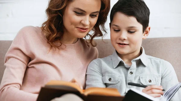 Sorrindo mulher lendo livro em primeiro plano borrado com filho — Fotografia de Stock
