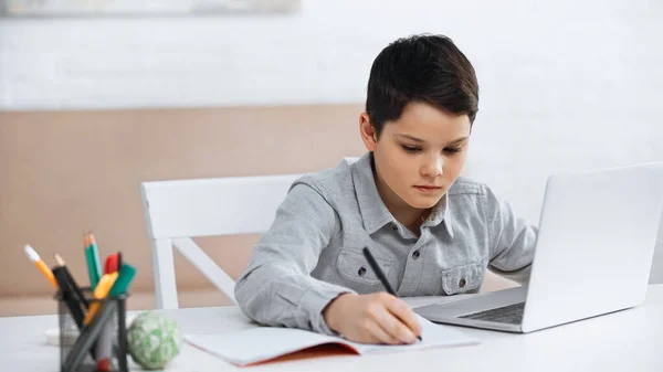 Підліток пише нотатки біля ноутбука під час онлайн-освіти — стокове фото