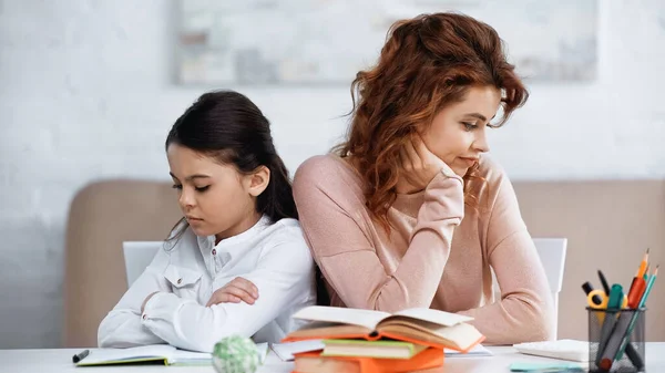Sad mother and daughter sitting near books on blurred foreground — Stock Photo
