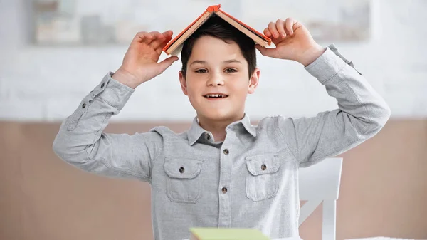 Усміхнений підліток тримає книжку над головою вдома. — стокове фото