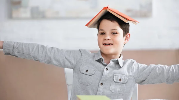 Positive preteen boy with book on head looking at camera — Stock Photo