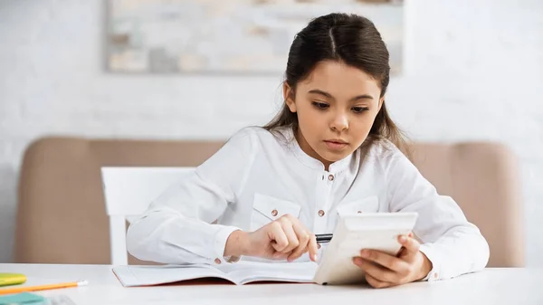 Підліткова дівчинка використовує калькулятор біля зошита та будинку. — стокове фото