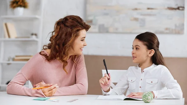 Sorridente madre sostenere figlia con i compiti a tavola — Foto stock