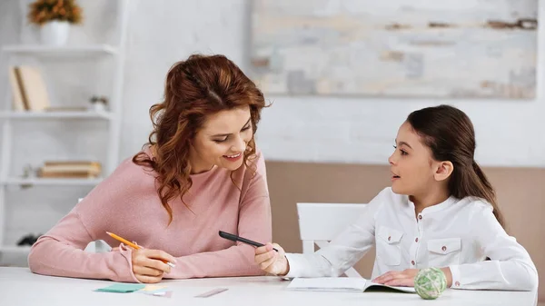 Kid with pen talking to mother near notebook and stationery — Stock Photo