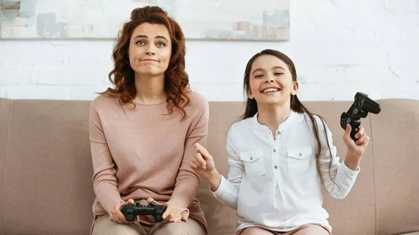 KYIV, UKRAINE -  APRIL 15, 2019: Smiling daughter holding joystick near sad mother on couch — Stock Photo