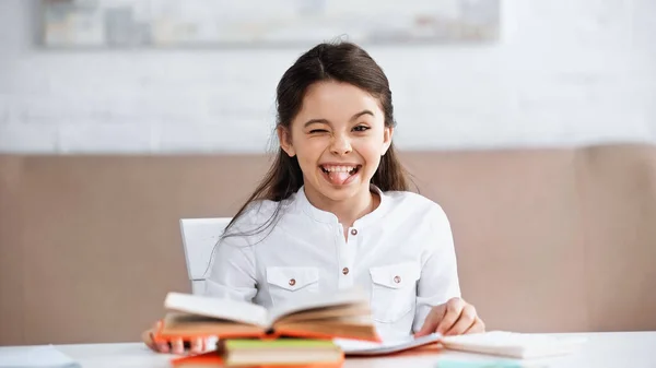 Preteen kid streckt die Zunge in der Nähe von Büchern auf verschwommenem Vordergrund — Stockfoto