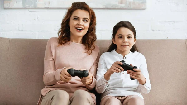 KYIV, UCRAINA - 15 APRILE 2019: Madre sorridente che gioca al videogioco vicino alla figlia adolescente sul divano — Foto stock