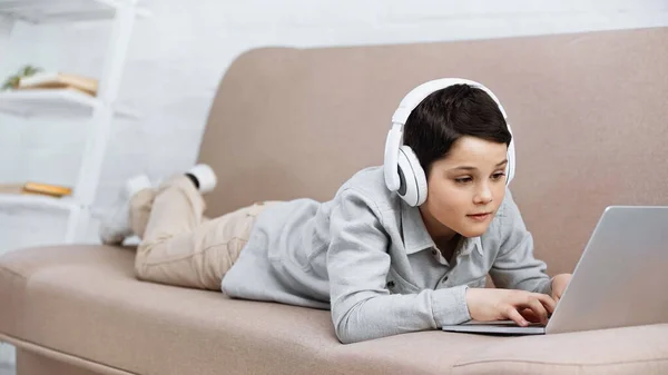 Підліток у навушниках за допомогою ноутбука на дивані. — стокове фото