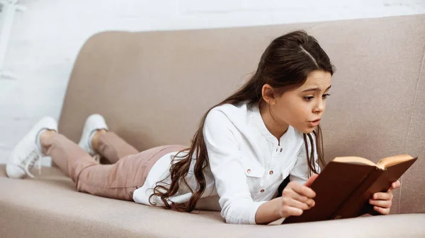 Preteen menina ler livro em primeiro plano desfocado em casa — Fotografia de Stock