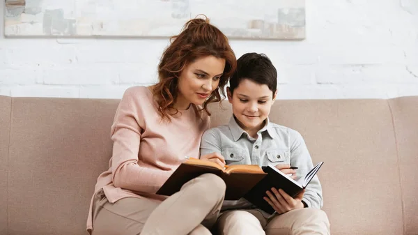 Madre e hijo leyendo libro durante la educación en el hogar - foto de stock