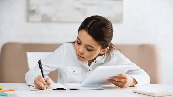 Preteen fille écrit sur ordinateur portable et en utilisant une tablette numérique pendant l'éducation en ligne — Photo de stock