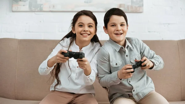KYIV, UCRANIA - 15 DE ABRIL DE 2019: Muchacha sonriente jugando videojuegos con su hermano en la sala de estar - foto de stock