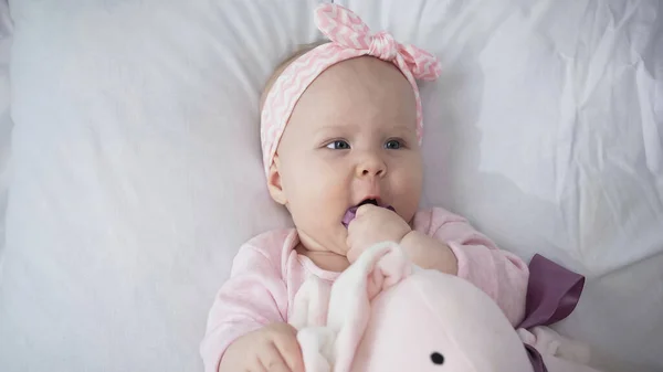 Top view of cute infant sucking fingers near soft toy — Stock Photo