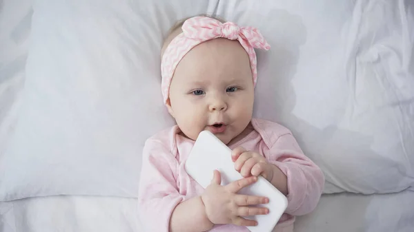 Top view of infant baby holding smartphone in bedroom — Stock Photo