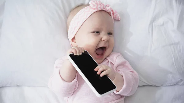 Top view of excited infant baby holding smartphone with blank screen — Stock Photo