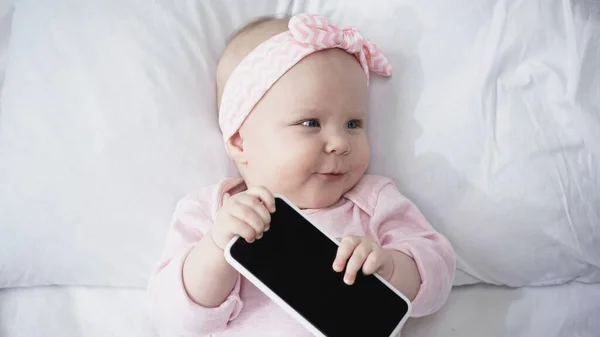 Top view of infant baby holding smartphone with blank screen and looking away — Stock Photo