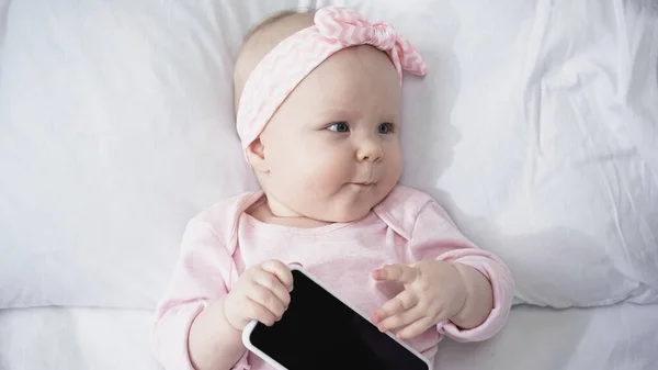Top view of infant girl holding smartphone with blank screen while looking away — Stock Photo
