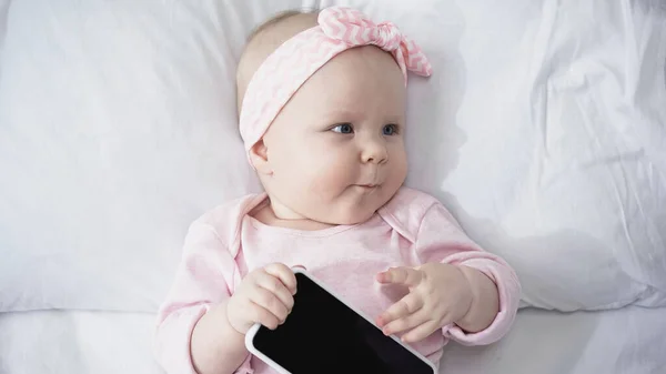 Vista dall'alto della bambina che tiene lo smartphone con lo schermo vuoto mentre distoglie lo sguardo — Foto stock