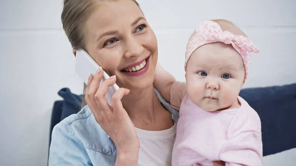 Счастливая мать разговаривает на смартфоне, держа в руках младенца дочь — стоковое фото
