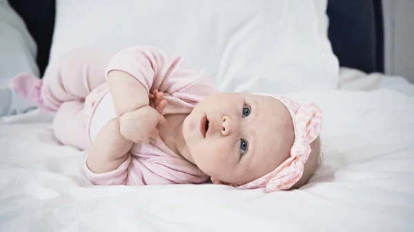 Bebê menina deitada na cama enquanto olha para cima — Fotografia de Stock