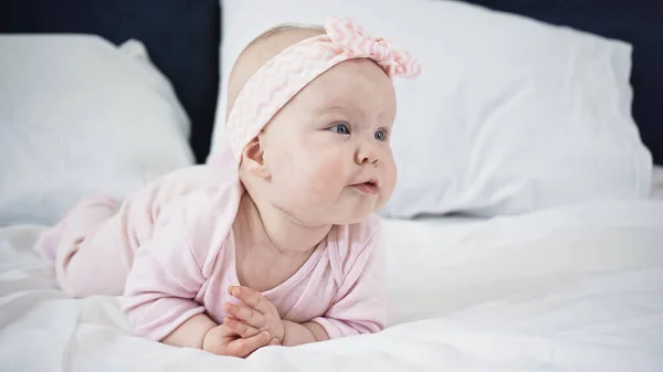 Bebê menina deitada na cama enquanto olha para longe — Fotografia de Stock