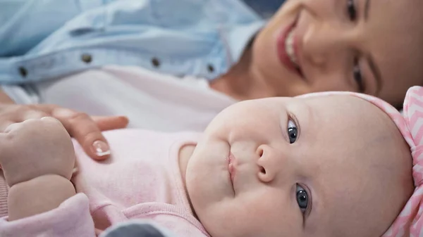 Baby-Mädchen blickt in Kamera, während es in der Nähe der Mutter auf verschwommenem Hintergrund liegt — Stockfoto