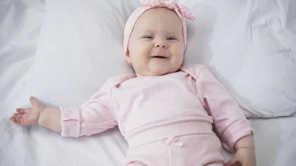 Vue du dessus de la jeune fille souriante dans le bandeau couché sur la literie blanche — Photo de stock