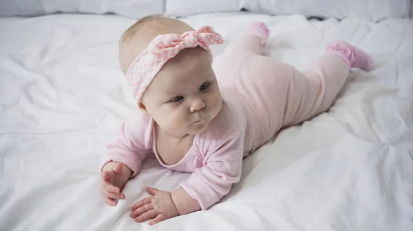 Bambina in fascia con fiocco sdraiata sul letto — Foto stock