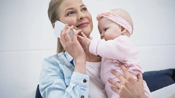 Femme souriante parlant sur un téléphone portable tout en tenant dans les bras fille enfant — Photo de stock