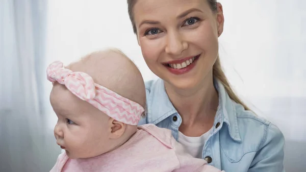 Donna felice che tiene in braccio figlia neonata in fascia con fiocco — Foto stock