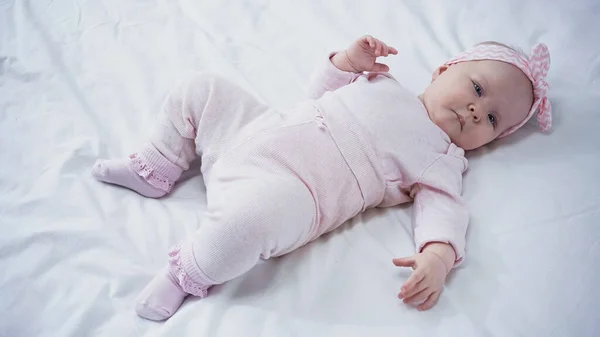 High angle view of baby girl in headband with bow lying on bed — Stock Photo