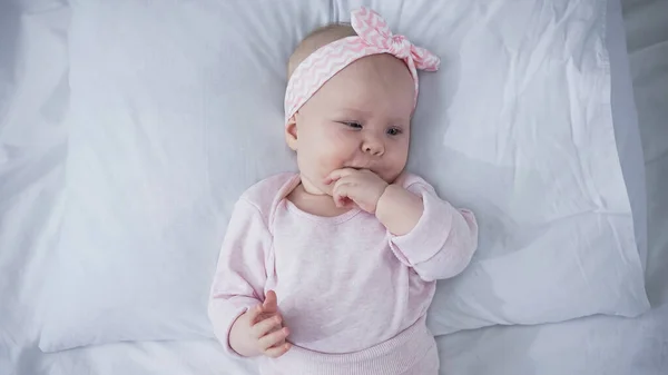 Vue du haut du bébé avec bandeau couché sur le lit et doigts suceurs — Photo de stock