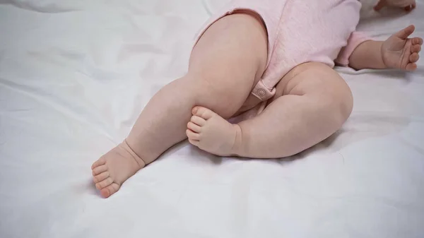 Vista parziale del bambino in pagliaccetto a piedi nudi sdraiato sul letto — Foto stock