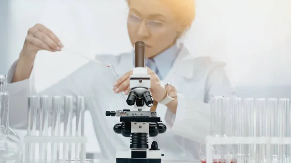 Microscope near african american scientist in glasses holding sample on blurred background — Stock Photo