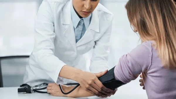 Vista recortada del médico afroamericano en bata blanca que mide la presión arterial de la mujer en la clínica — Stock Photo