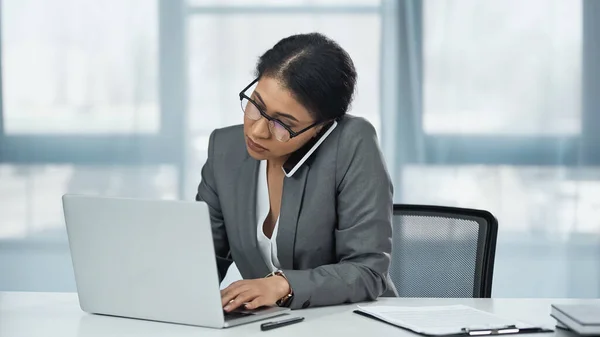 Afro-américaine femme d'affaires parlant sur téléphone mobile près d'un ordinateur portable sur le bureau — Photo de stock