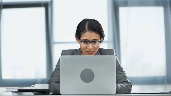 Smiling african american businesswoman in glasses looking at laptop — Stock Photo