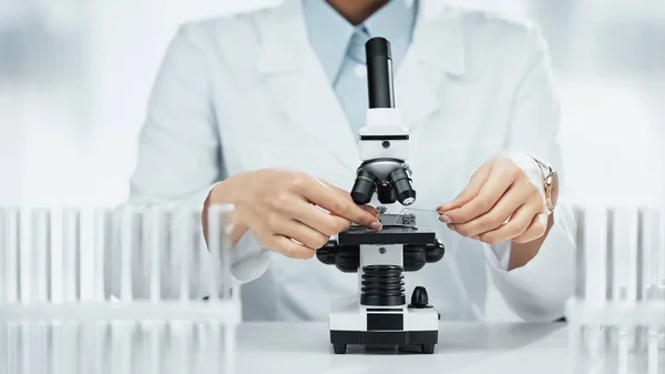 Cropped view of african american scientist holding glass with sample near microscope in lab — Stock Photo