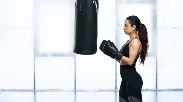 Vista lateral del entrenamiento de la deportista con saco de boxeo en el gimnasio - foto de stock