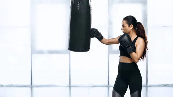 Side view of young sportswoman training with punching bag in gym — Stock Photo