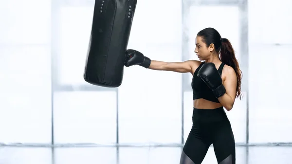 Vue latérale de l'entraînement ciblé des sportives avec sac de boxe dans la salle de gym — Photo de stock