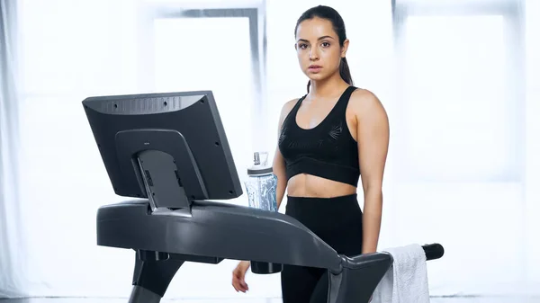 Sporty woman in sportswear on treadmill near sports bottle with water in gym — Stock Photo