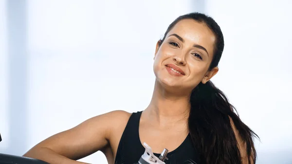 Mujer feliz y deportiva sosteniendo botella de deporte con agua en el gimnasio - foto de stock