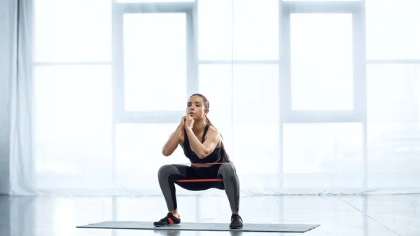 Mujer joven y sudorosa haciendo ejercicio con banda de resistencia en el gimnasio - foto de stock