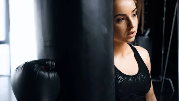 Tired sportswoman in boxing glove leaning on punching bag — Stock Photo