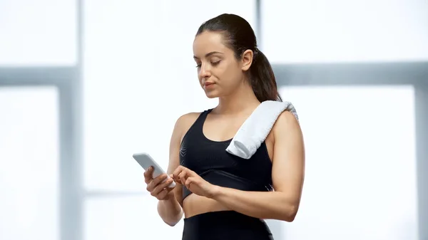 Jeune sportive avec serviette textos sur smartphone dans la salle de gym — Photo de stock