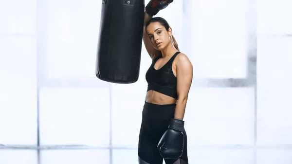 Sportive épuisée en gants de boxe penchée sur le sac de boxe dans la salle de gym — Photo de stock