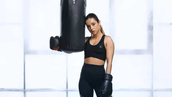 Femme de sport épuisée en gants de boxe et vêtements de sport s'appuyant sur le sac de boxe dans la salle de gym — Photo de stock